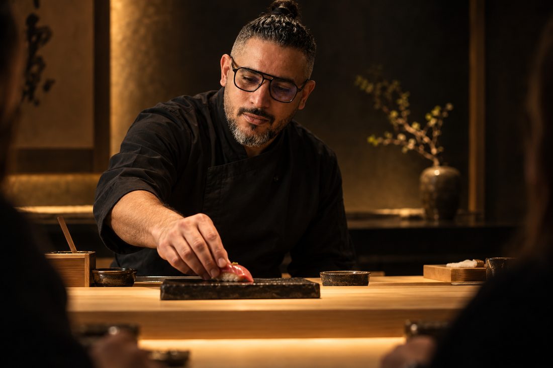 Chef Aziz placing nigiri on a black stone plate behind a hinoki counter