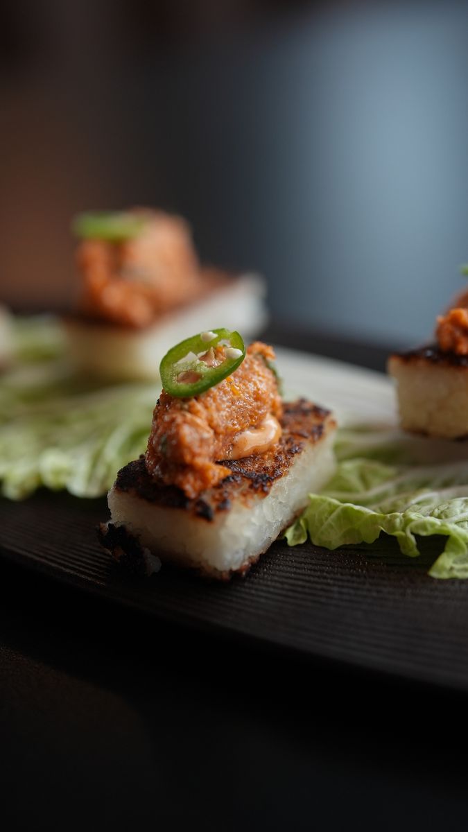 Crispy rice squares topped with jalapeño on a black plate
