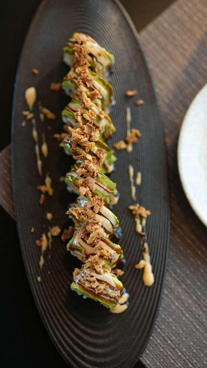 An avocado roll with a crisp topping on a ridged plate