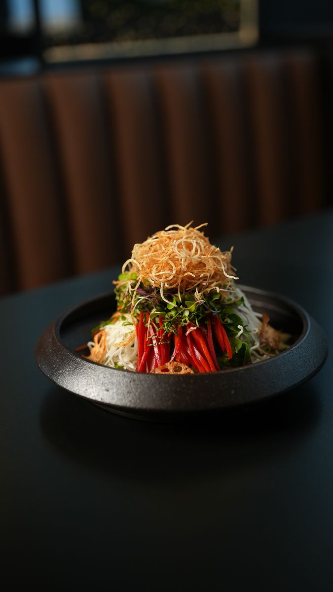 A salad under a nest of crisp noodles in a black bowl