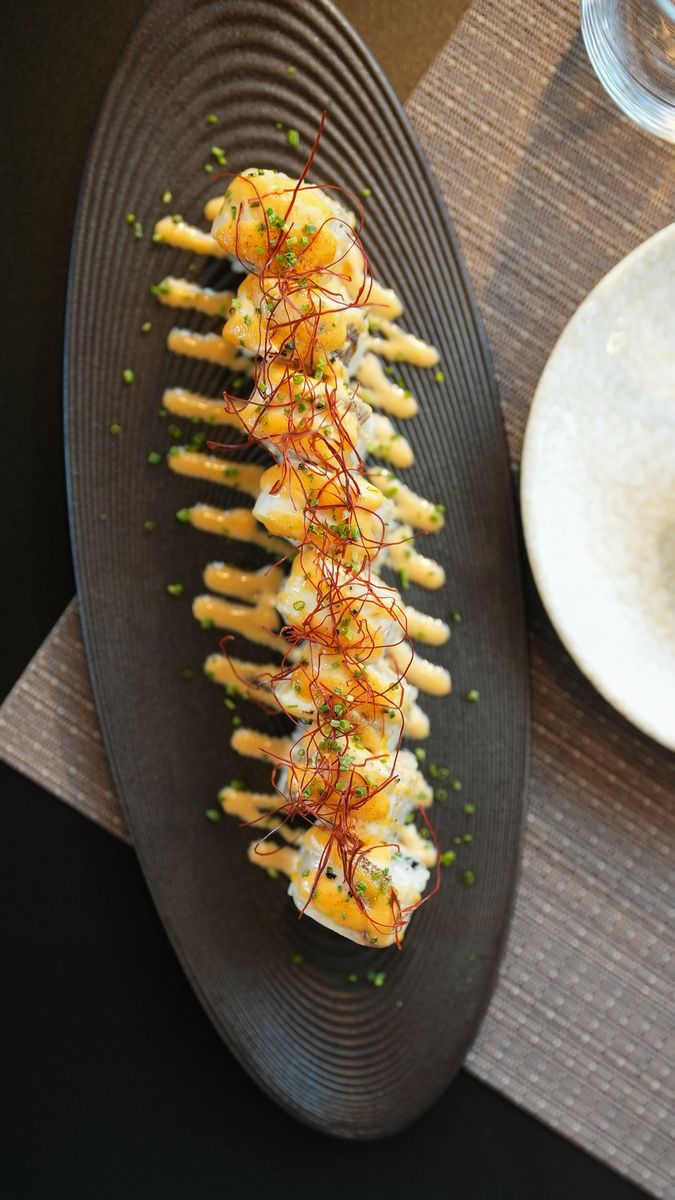 A torched sushi roll on a black plate