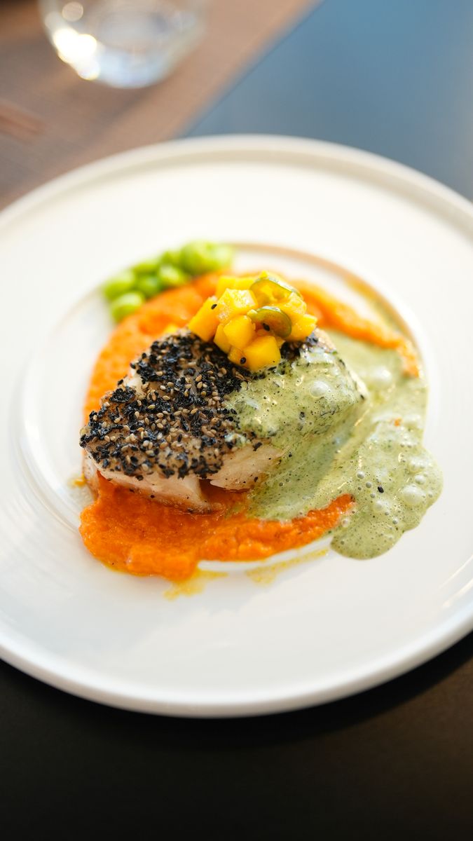 Sesame-crusted fish with two sauces and mango on a white plate